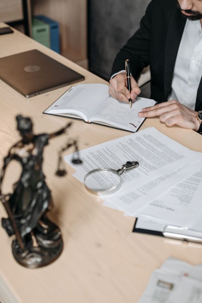 pexels photo 8112121 Professional working on documents at desk with legal statue and magnifying glass.